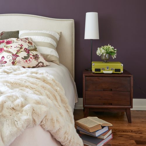 bedroom image with upholstered headboard and faux fur throw - deep purple aubergine wall colour - cream neutral bed linens pattern play - linda mazur design