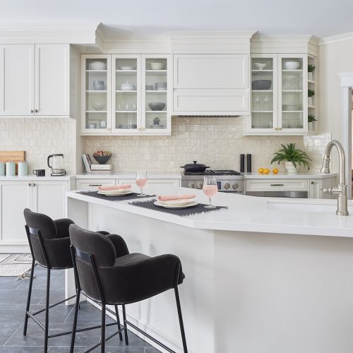 markham luxury family kitchen renovation - cream white custom millwork cabinets and range hood with glass cabinets - white quartz waterfall countertops black porcelain flooring - velvet counter stools CB2 with angled peninsula instead of island- design build renovate linda mazur design toronto canada designer